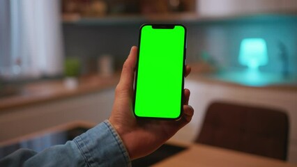 Caucasian man looking at smartphone with green screen. Close-up shot of male hands with mobile phone. Chroma key, mockup concept. Modern technology. Indoors