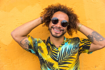 Attractive man with afro hair in summer summer in a palm tree shirt on a yellow background