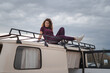 © ADDICTIVE STOCK - Smiling woman resting on van top with luggage carrier