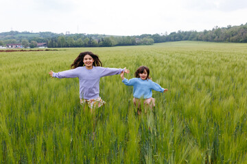 two girls running together in a big field of wheat