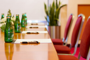 close up photo of a a long table in a hotel conference room with a bunch of bottles, sheets and pens on it, ready for meeting