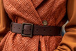 Fancy details of orange textured coat with leather brown belt. Autumn casual fashion style