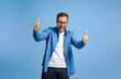 © Moon Safari - Successful businessman showing thumbs up and shouting ecstatically against blue background