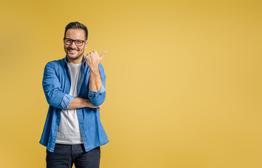 Portrait of smiling businessman pointing thumb at copy space for marketing over yellow background