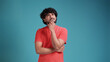 © Виталий Лысак - swarthy man in coral t-shirt on blue studio background thinking pondering looking for an idea.