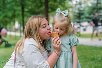 Little cute girl in green summer dress eating delicious ice cream with mom in city park summer family lifestyle Childhood