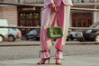Street fashion details: woman wearing trendy pink suit trousers, high heeled strap sandals, carrying green color faux reptile leather bag. Copy, empty space for text
