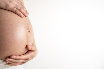 Wall Mural - Pregnant woman gently holding her naked round belly with her hands in final month of pregnancy. Third trimester - week 36. Close up. Side view. White background. Bright shot.