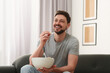 © New Africa - Happy man with bowl of popcorn watching movie via TV on sofa at home