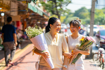 Happy Asian family mother and daughter holding flower bouquet walking together during shopping at florist shop street market in the city for flowers vase arrangement on spring summer holiday vacation.