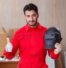 Wall Mural - Young repairman with a welding gun electrode and a helmet weldin