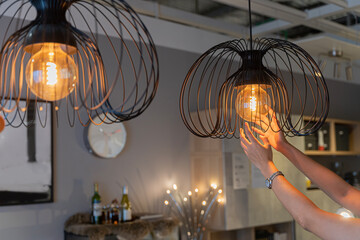 Woman changing light bulb in hanging lamp at home. House owner cleaning or changing vintage light bulb. House maintenance concept.