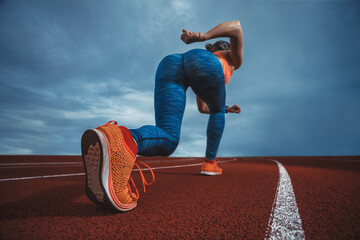 Close up wide angle view of a female sprinter athlete getting ready to start a race on a tartan racetrack