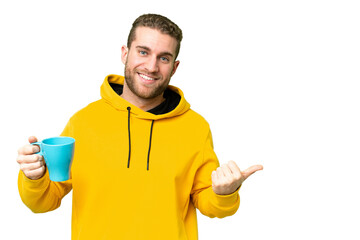 Wall Mural - Young handsome blonde man holding cup of coffee over isolated background pointing to the side to present a product