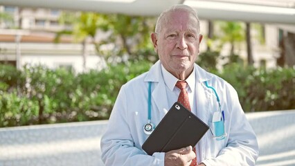 Canvas Print - Senior grey-haired man doctor smiling confident holding touchpad at park