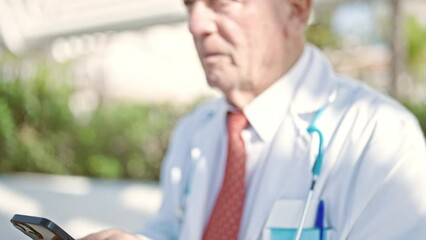 Wall Mural - Senior grey-haired man doctor standing with serious expression using smartphone at park