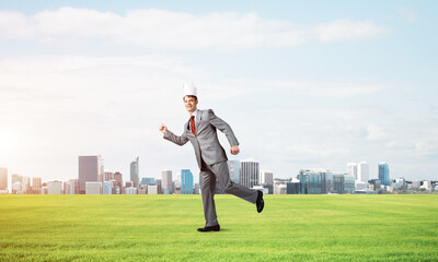 Wall Mural - King businessman in elegant suit running on green grass and modern cityscape at background