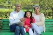 © Maahir - Grandparents enjoying with grand daughter in park surrounded with greenery and serenity. They are having joyful and cheerful time together in lush green environment. Loads of smile and happy moments.