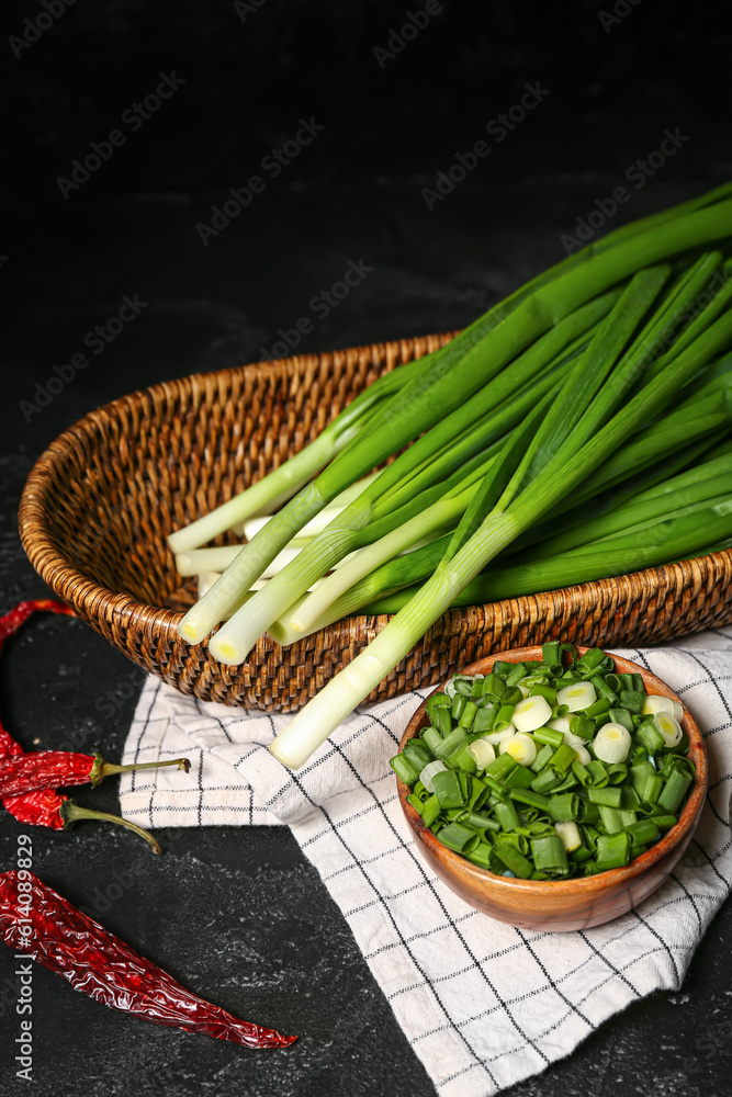 Bowl and wicker basket with fresh green onion on dark background