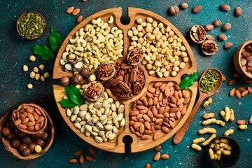 Wall Mural - Assortment of nuts on a wooden plate. Top view. Mixed nuts on wooden table. On a dark background.