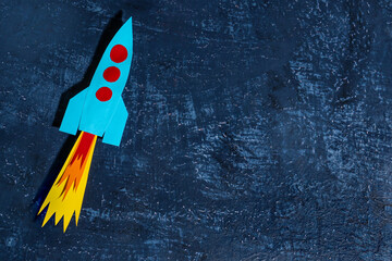 Blue paper rocket on dark grunge background