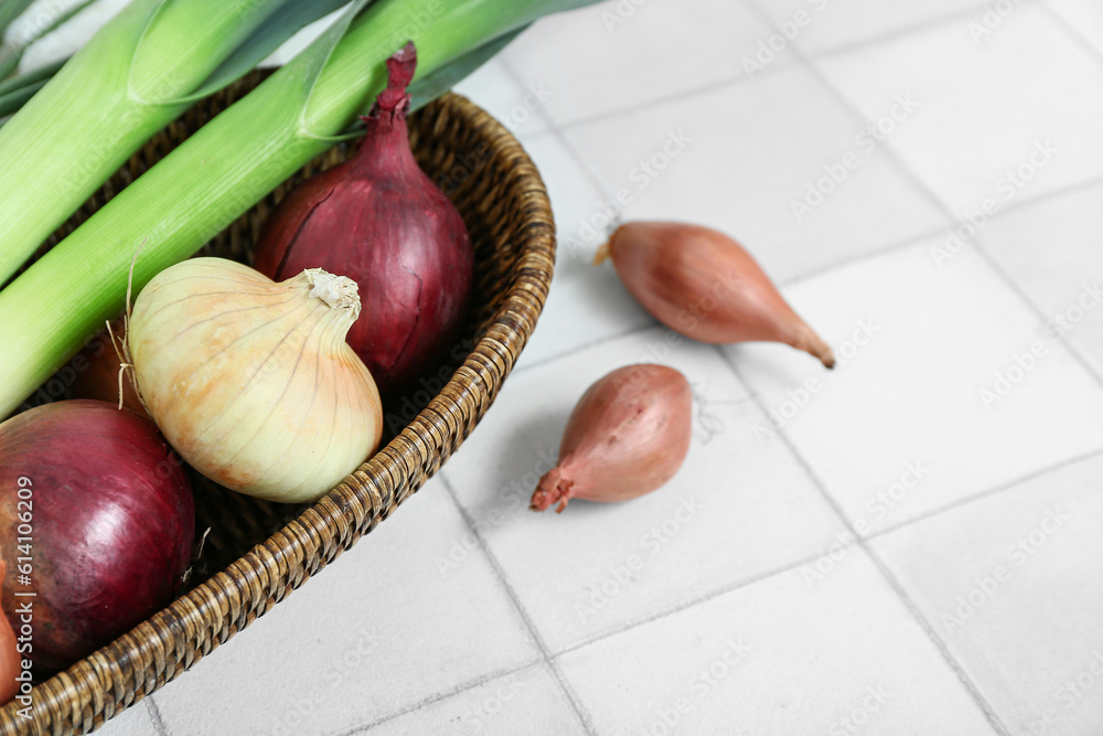 Wicker basket with different kinds of onion on light tile background, closeup