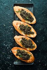 Wall Mural - Toasts with black caviar on a stone plate, caviar in a bowl. On a black stone background. Rustic style.