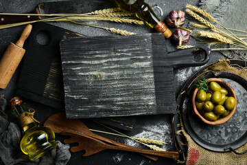 Wall Mural - Kitchen cutting board, olives and oil. On a black stone background. Top view.
