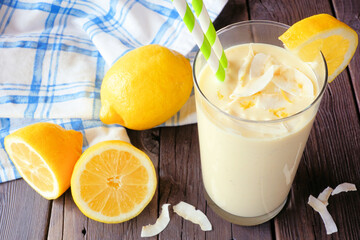 Wall Mural - Summer lemon coconut smoothie. Close up table scene against a dark wood background.