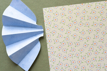 Wall Mural - fan folded blue scrapbook paper shape set near a sheet of paper with floral pattern