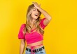 Young beautiful blonde woman wearing pink crop top over yellow  studio background surprised with hand on head for mistake, remember error. Forgot, bad memory concept.