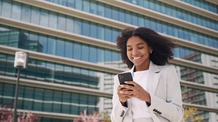 happy busy young african american business woman using mobile phone outdoors. smiling female profess