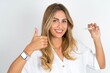 young beautiful woman wearing white shirt over white studio background holding an invisible braces aligner and rising thumb up, recommending this new treatment. Dental healthcare concept.