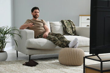 Wall Mural - Happy soldier watching TV on sofa in living room. Military service