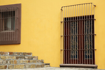 Wall Mural - Yellow building with wooden door and window behind steel grilles outdoors