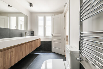 Newly installed designer bathroom with tall wooden cabinet with elongated drawers, two white porcelain one-piece