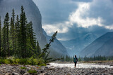 Fototapeta  - Hiking in the rain Woman Hiker crosses the Ghost River Trans Alta trail with Mt Aylmer in the background