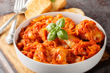 Pieces of white sea fish stewed with vegetables in tomato sauce served with toast close-up on a wooden board on the table. horizontal