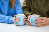 Fototapeta  - Dwie osoby trzymające w dłoniach kubki z herbatą siedzące przy stoliku w kafejce, z bliska 