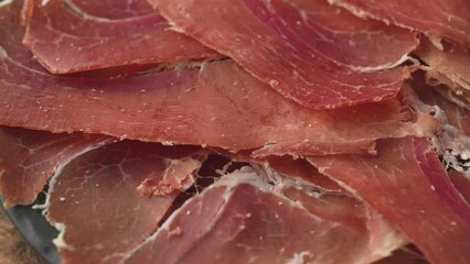 Poster - plate of sliced spanish iberico ham on wooden table background, rotating