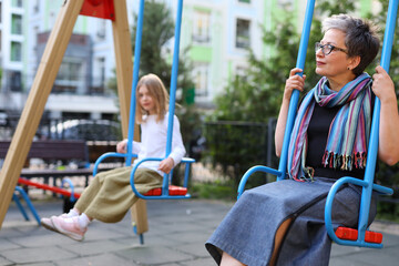 Sticker - Senior woman rides on a swing with a girl child, selective focus.