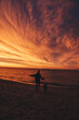 Frau und Hund gemeinsam am Strand und erleben einen wunderschönen Sonnenuntergang am Meer mit leuchtendem Himmel