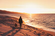 Frau und Hund gehen am Strand spazieren und erleben einen wunderschönen Sonnenuntergang am Meer 