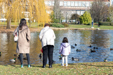 Three Generations Of Women, Daughter, Mother And Grandmother, Feeding The Ducks, Viewed From Behind