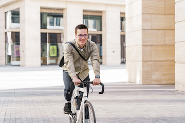 A smiling man in formal attire arrived at work in the office on a bicycle. The guy with the business bag uses environmentally friendly transport.