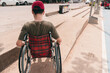 Behind of young man with disability pushing wheelchair up ramp on the sidewalk of public road by himself, Concept of facilities for disabilities people to live as part of society with happy and safety