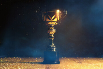 Wall Mural - low key image of trophy over wooden table and dark background, with abstract glitter lights