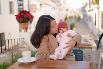 young happy and beautiful asian chinese woman holding her adorable little baby girl while having cof