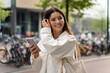 © Andrei - Sustainable young multiethnic woman wearing white eco clothes and a shopper holding a phone walking in the street filled with bicycles in the background
