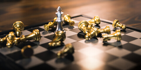 Silver chess king standing among golden falling chess pieces, business competition has winners and losers, strategy will make company successful, investment and management concept.